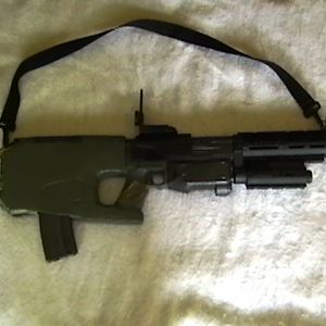 CARB weapon system in shotgun mode. Slung under the barrel is a red spot/laser designator. Magazine is not canon; it is a 30-round M16/M4 magazine.