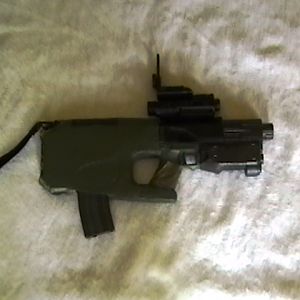 CARB weapon on carbine mode. On top of the receiver is a red spot/laser designator. The magazine is an M16/M4 magazine.